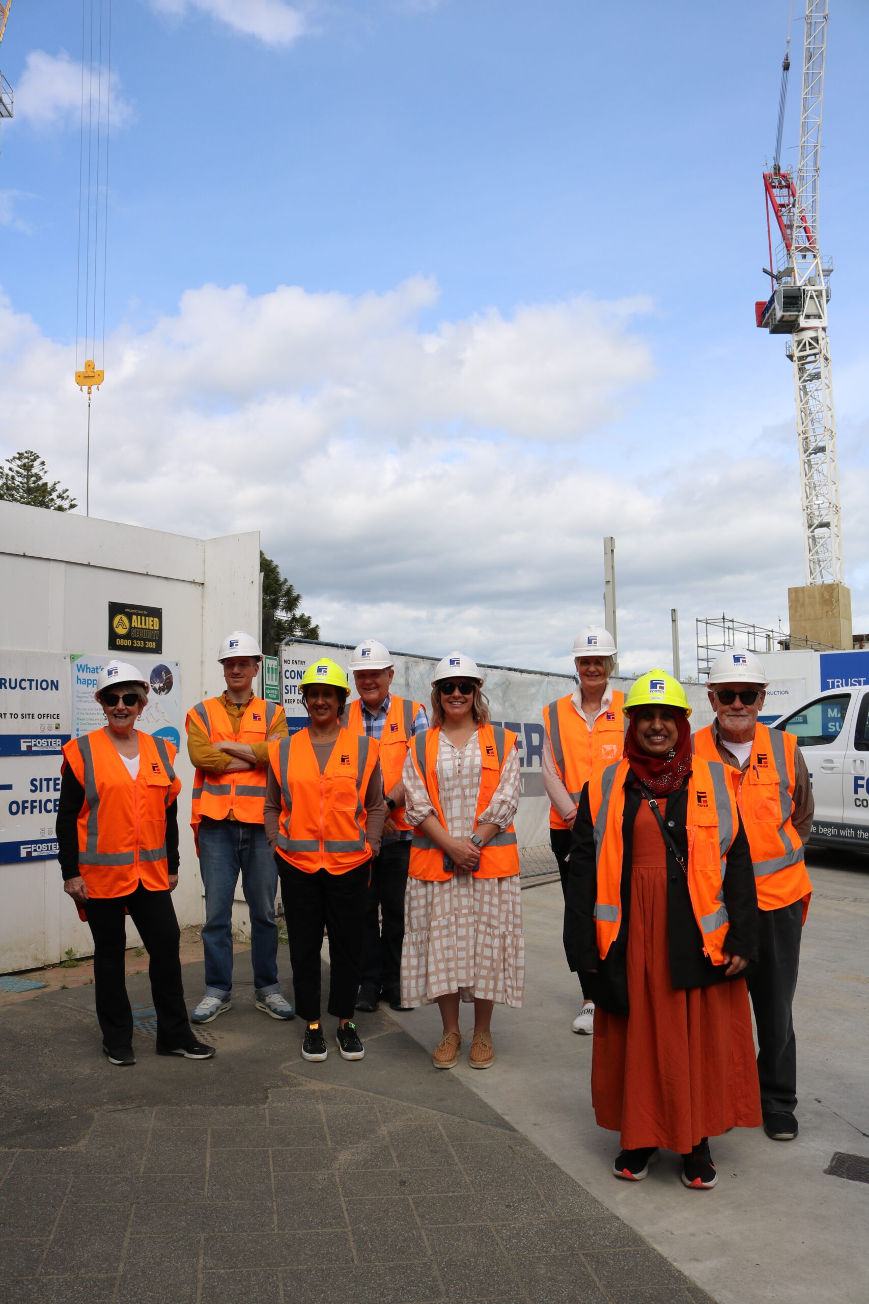 Trustees standing outside the Waikato Regional Theatre construction site wearing hi-vis vests and hard hats, with a crane in the background.