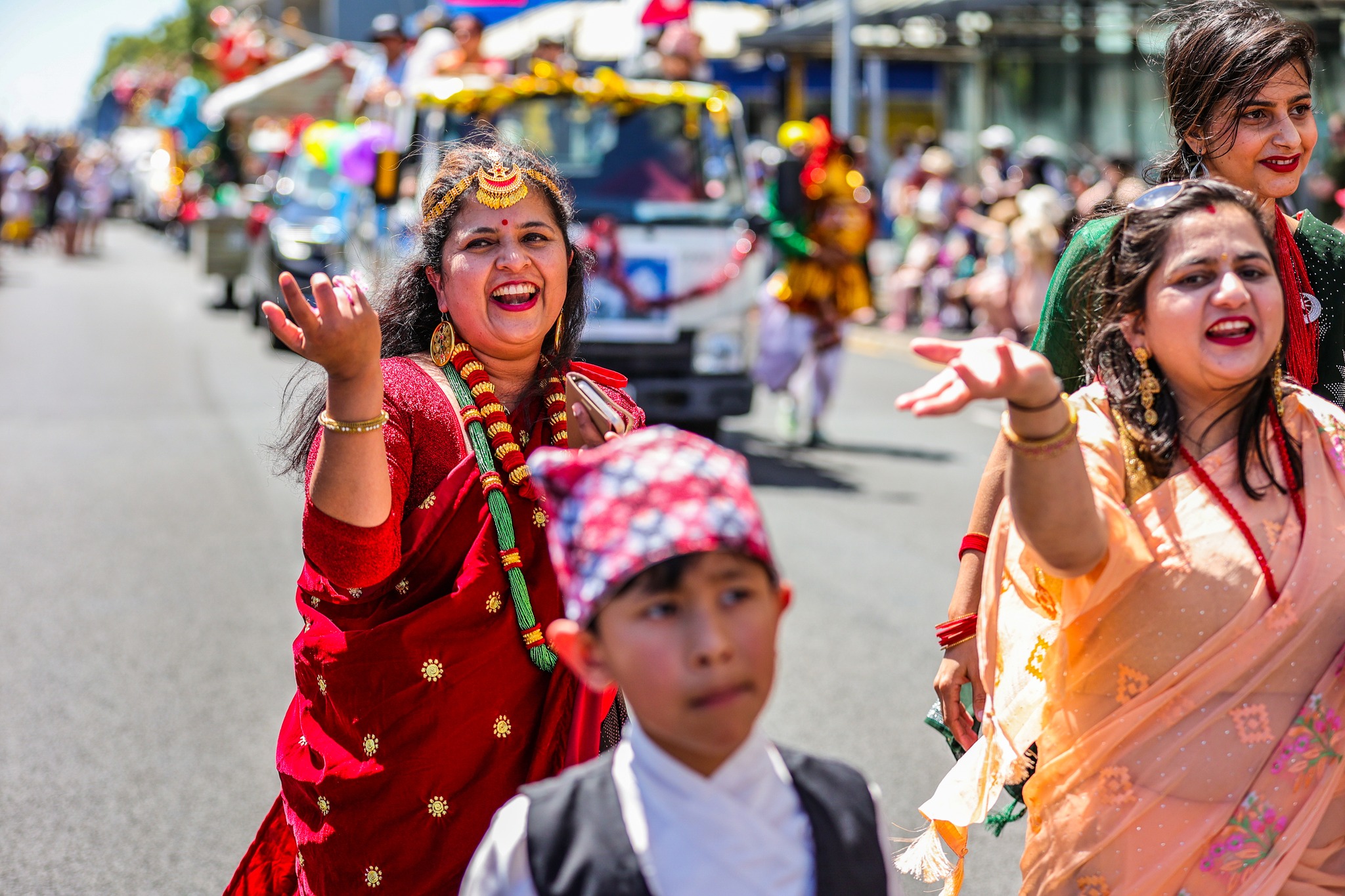 Indian women in colourful clothing dancing and smiling in the road with parade blurred in the background
