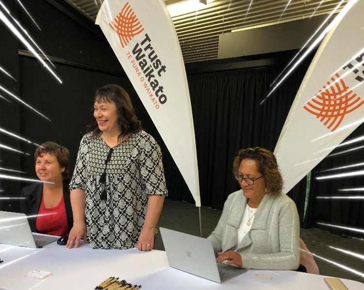 Nita, Tarita and Rongo from the Grants team at an event with Trust Waikato flags in the background.