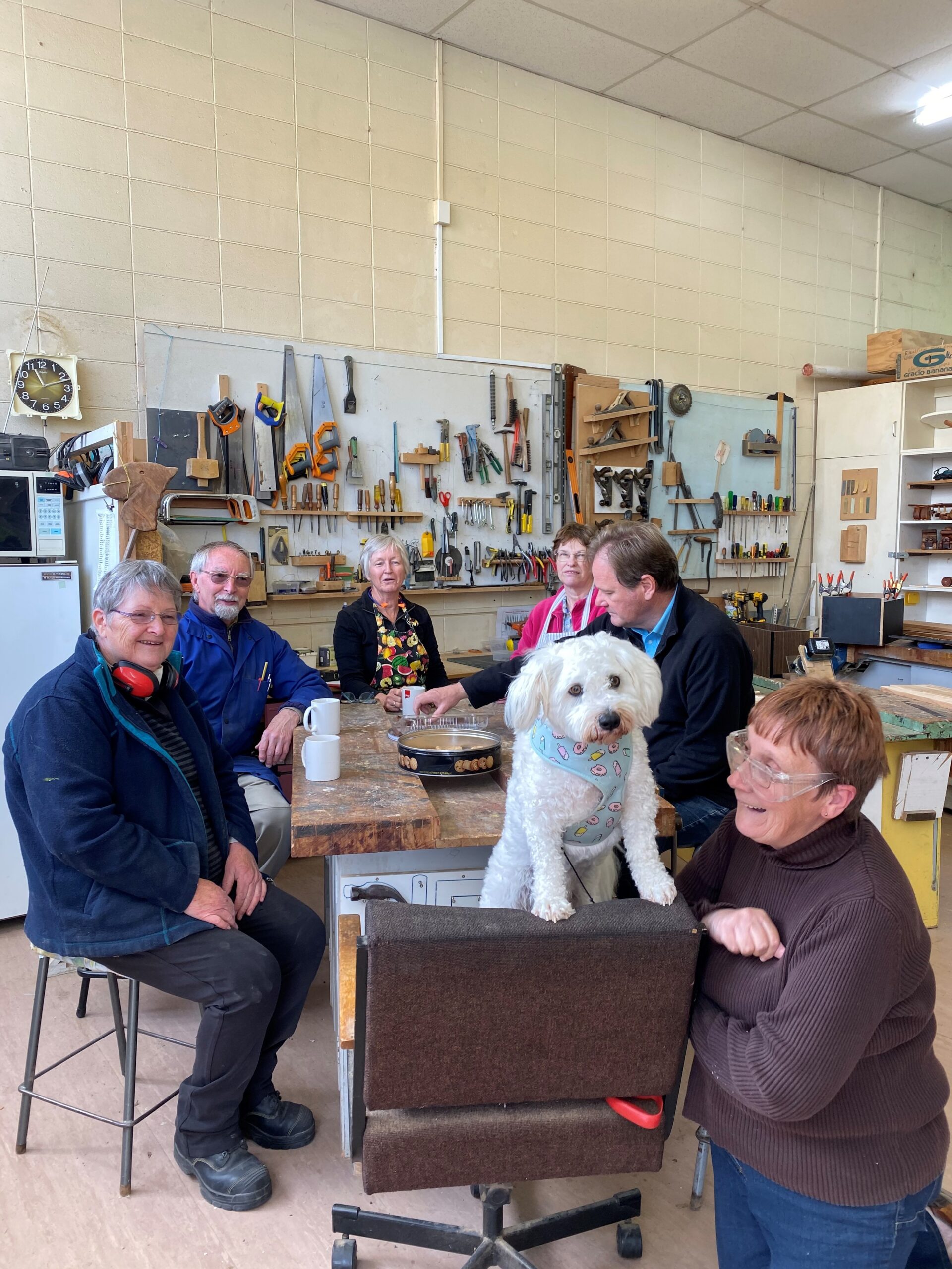 Group of elderly people and a dog having morning tea at woodworking workshop