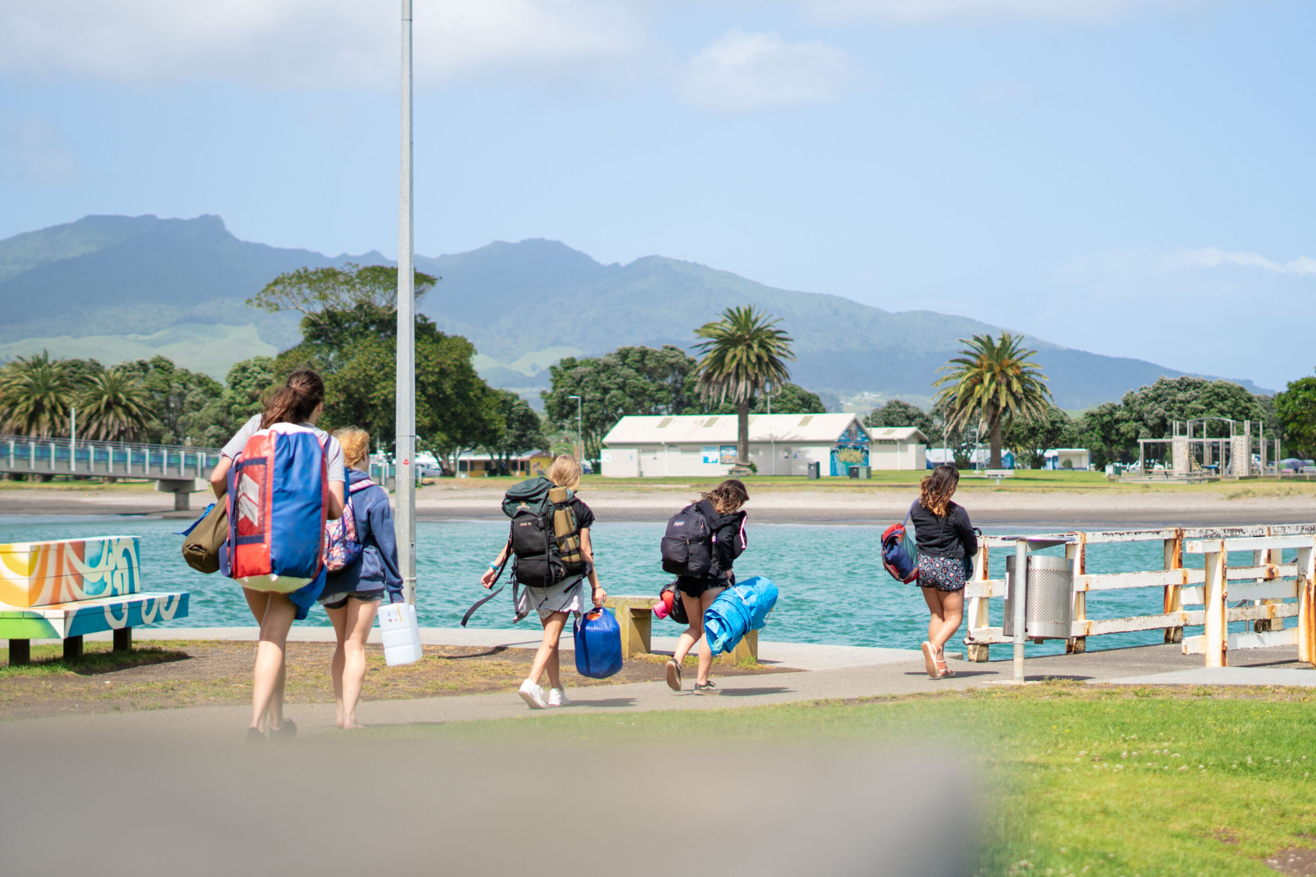 Group of girls with camping gear walking towards the campground in Raglan