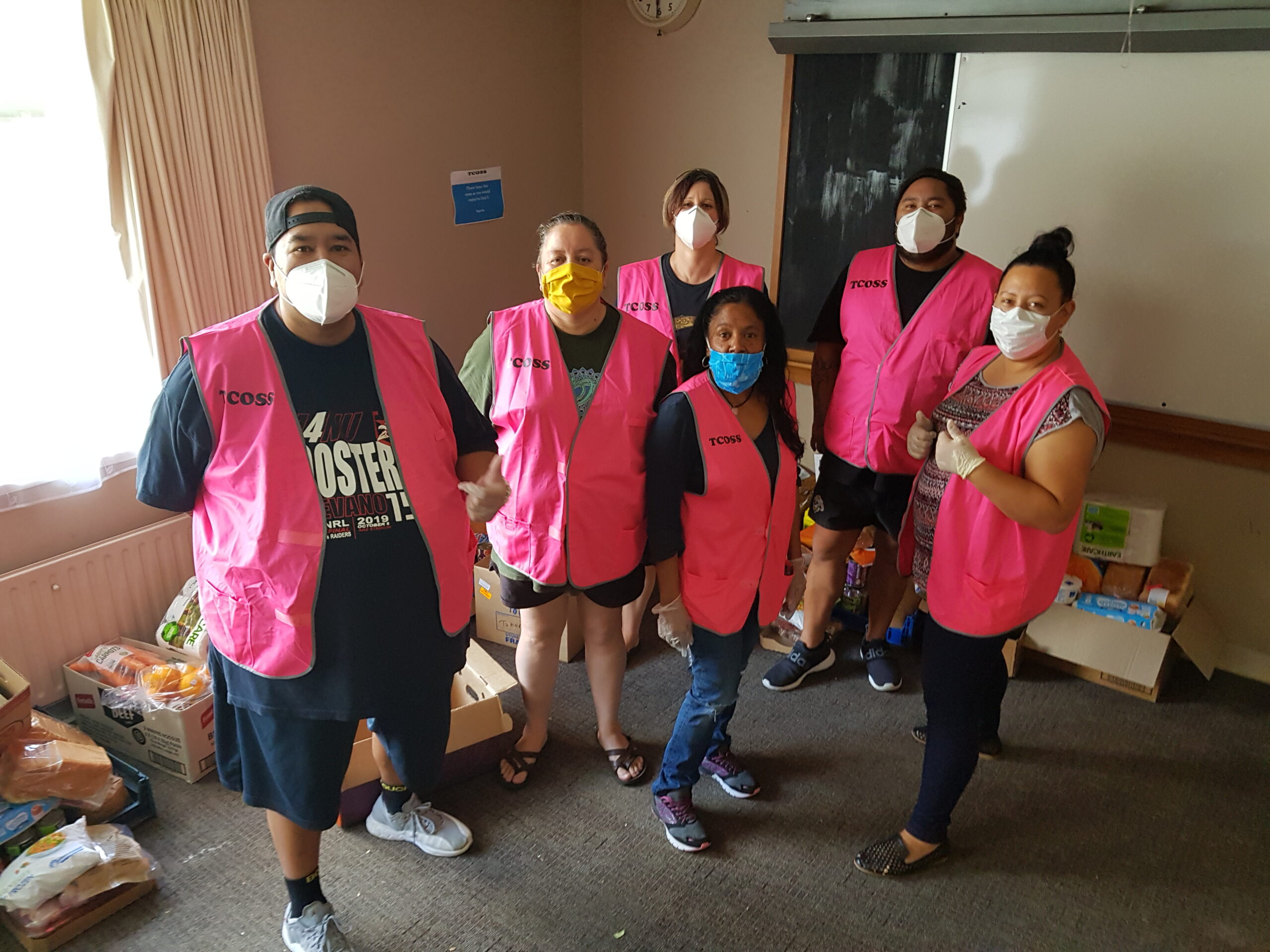 Group of volunteers wearing masks and pink hi vis vests with food parcels in the background