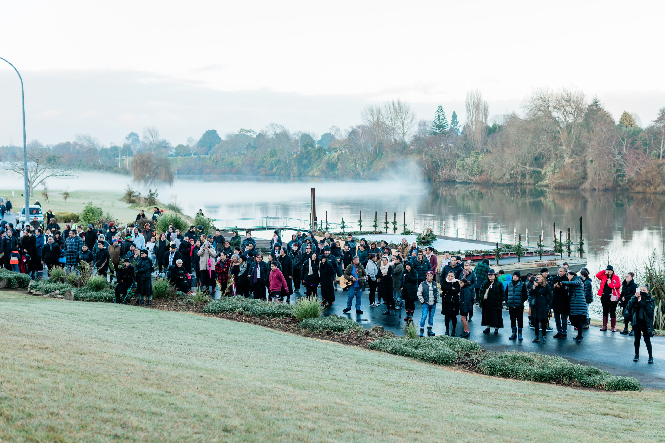Crowd of people along the Waikato river bank on a foggy morning